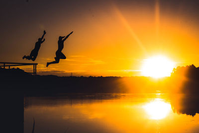 Silhouette of jumping over lake against sky during sunset