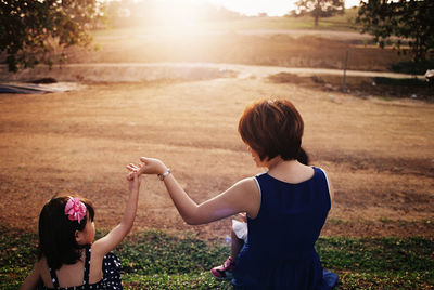 Rear view of mother and daughter holding hands while sitting on field during sunset
