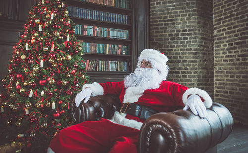 Man wearing santa claus costume sitting on armchair at home