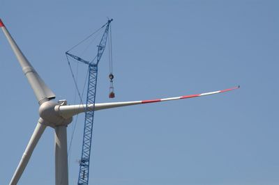 Low angle view of crane and windmill against clear sky