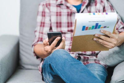 Midsection of woman using mobile phone while sitting on sofa