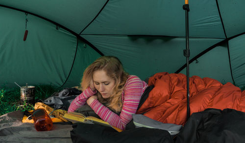 Young woman reading book in camp tent