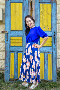 Portrait of a smiling young woman standing against blue wall