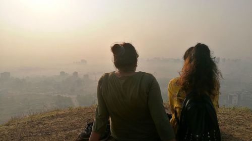 Rear view of women sitting on field during foggy weather