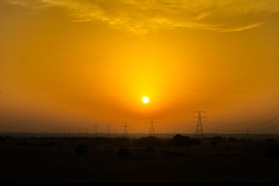 Silhouette electricity pylon against orange sky