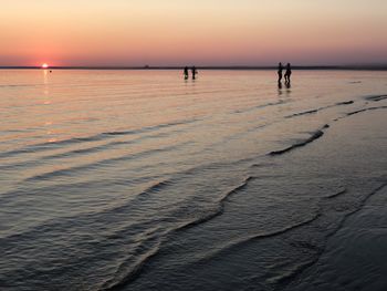 Silhouette people on beach against sky during sunset