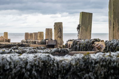 Damaged pier at shore against cloudy sky