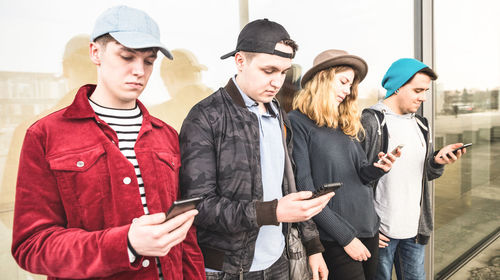 Friends using mobile phone while standing against wall