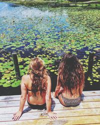 Rear view of female friends sitting on pier over lake