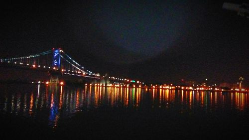 Illuminated bridge over river against sky at night