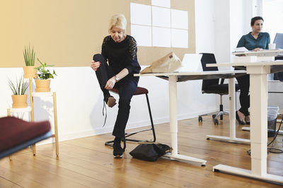 Senior female professional tying shoelace while sitting at creative office