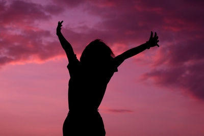 Silhouette woman with arms raised against sky during sunset