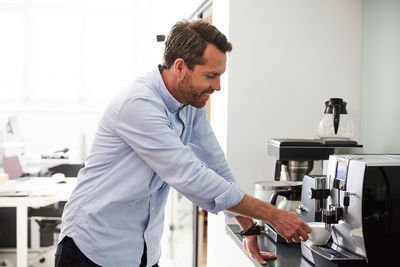 Businessman using coffee maker at kitchen counter in creative office