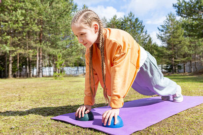 A teenage girl goes in for sports in nature, on a sunny summer on a sports mat. 