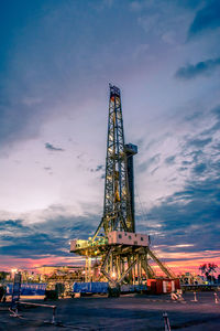 Low angle view of drilling rig against sky during sunset