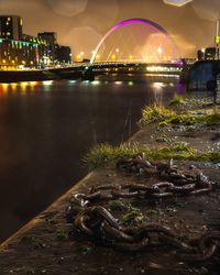 Illuminated bridge over river by buildings in city at night