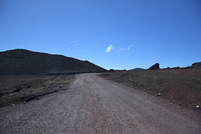 Dirt road on landscape against blue sky