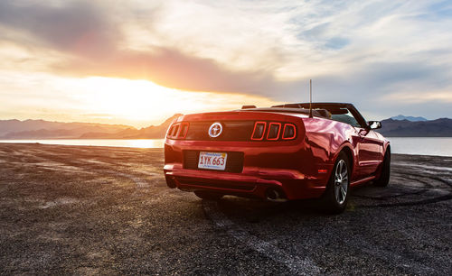 Red car on road against sky during sunset