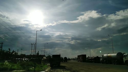 Vehicles on road against cloudy sky on sunny day