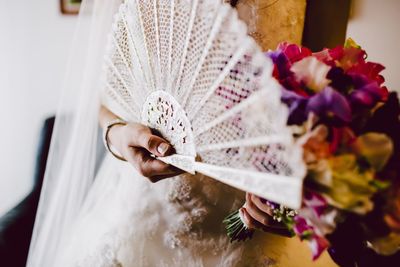 Midsection of bride holding fan and flower bouquet