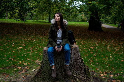 Full length of woman sitting on tree stump