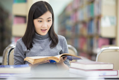Young woman reading book while sitting at table in library