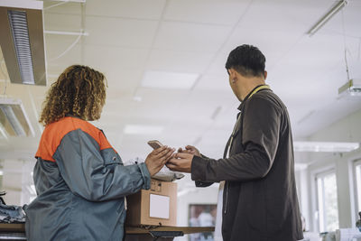 Low angle view of fashion designer looking away while receiving package from delivery person at workshop