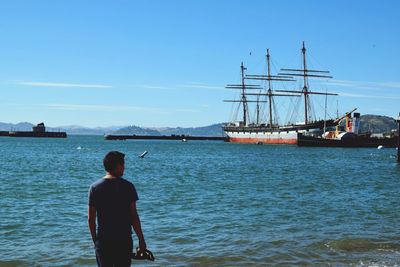 Rear view of man standing at harbor against clear sky