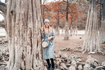 Woman standing by tree trunk in forest