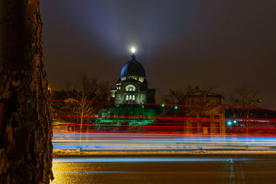 Light trails on illuminated building against sky at night