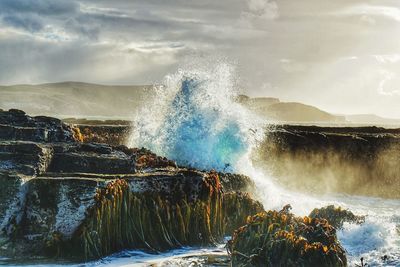 Waves splashing on rocks against the sky