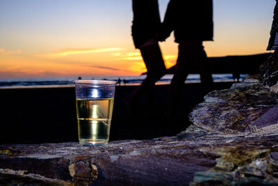 Low section of beer glass against sea at sunset