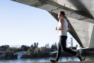 Man running by river under bridge