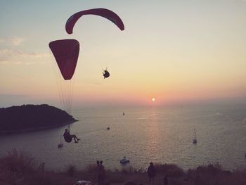 People paragliding over sea during sunset