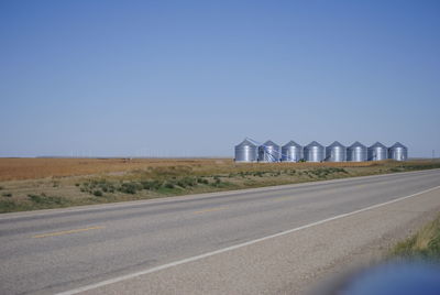 Empty road amidst field against clear blue sky