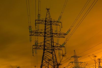 Low angle view of electricity pylon against sky during sunset