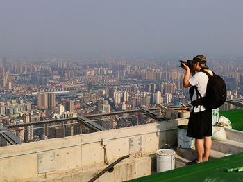 Side view of man with backpack photographing cityscape against sky