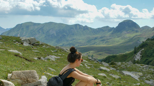 Woman sitting on mountain against sky