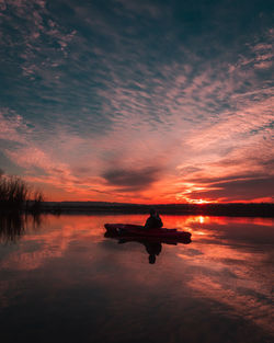 Silhouette woman on lake against orange sky