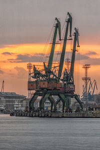 Cranes at commercial dock against sky during sunset