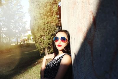 Portrait of young woman wearing sunglasses standing against trees