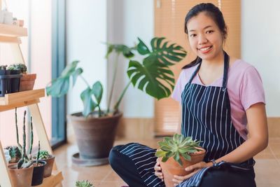 Portrait of young woman standing by potted plants