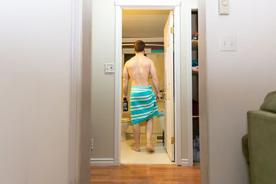 Rear view of shirtless man standing at entrance of home