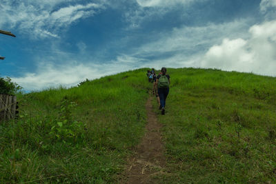 Rear view of men walking on field against sky