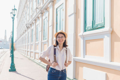 Portrait of smiling young woman standing against building in city