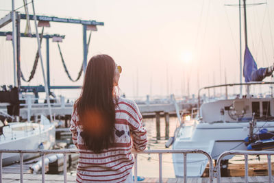 Rear view of woman standing at harbor against sky