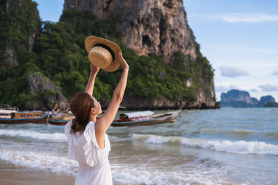 Rear view of woman standing at beach against sky