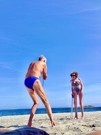 Full length of shirtless man standing at beach against clear blue sky