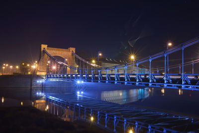 Illuminated bridge over river in city at night