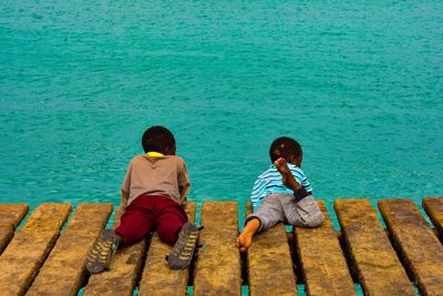 Rear view of couple sitting on bench by sea